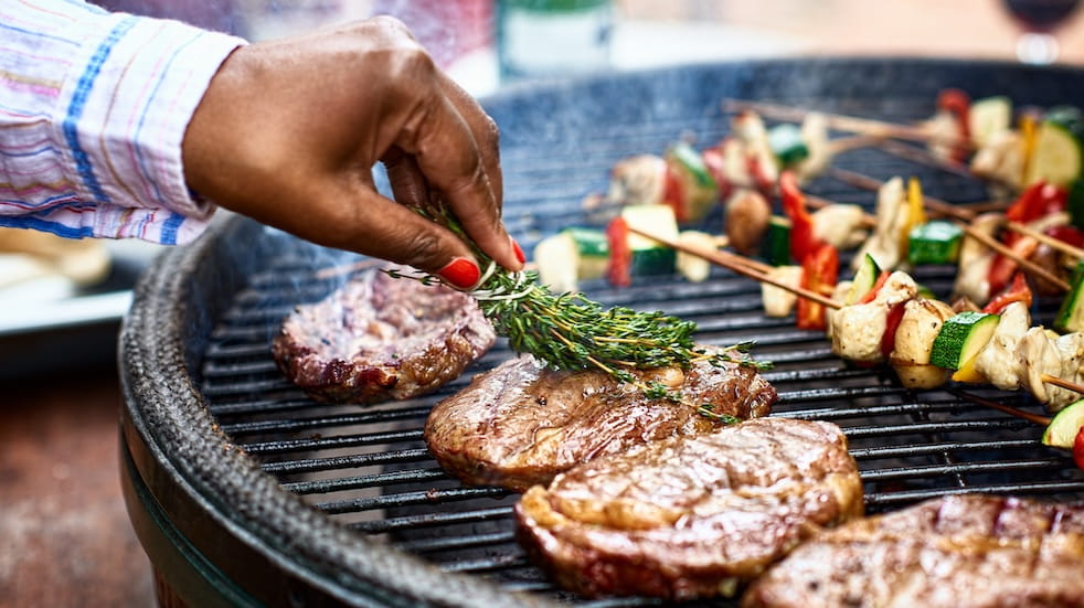 Woman's hand basting meat on barbecue with fresh herbs